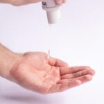 Crop anonymous male applying antibacterial gel on hand for daily hygiene routine and preventing spread of COVID